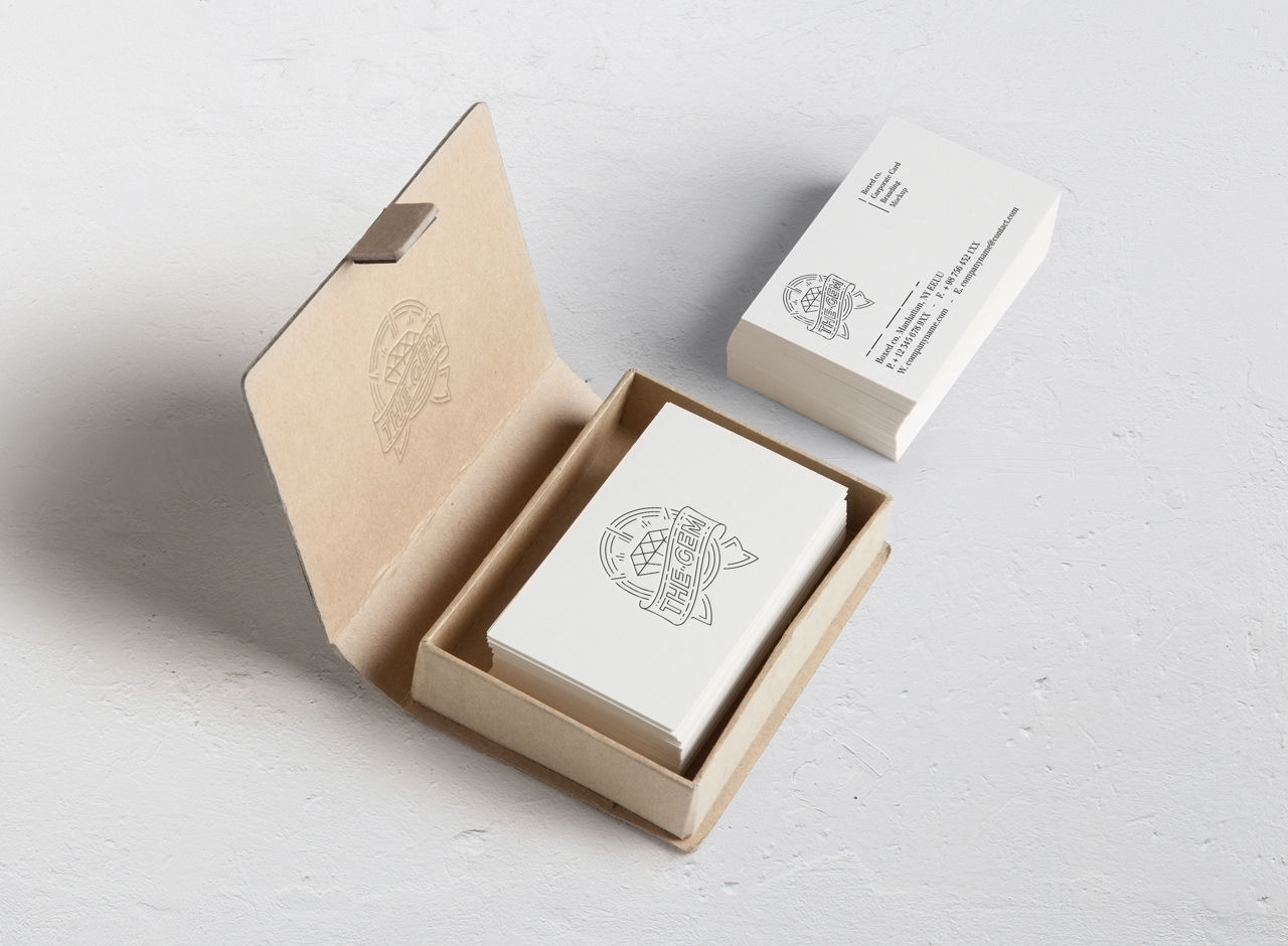 A stack of white business cards with a simple logo and text is shown; some cards are in a brown cardboard box while others are stacked outside on a white surface.