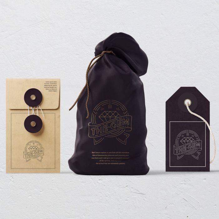 Three items with The Gem logo: a tan envelope with a string closure, a dark drawstring pouch, and a dark tag with a white string, all arranged against a plain white background.