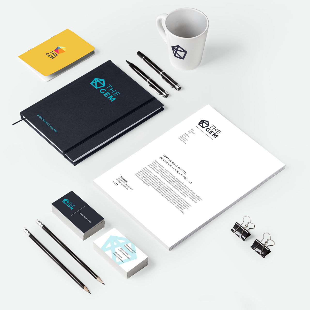 A flat lay of branded office items including a mug, notebooks, pens, pencils, binder clips, business cards, and a letterhead, all featuring The Gem logo in black, teal, and white on a white background.