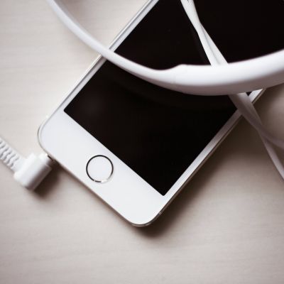 A smartphone with a black screen and a white frame lies on a light surface, partially covered by white wired headphones.