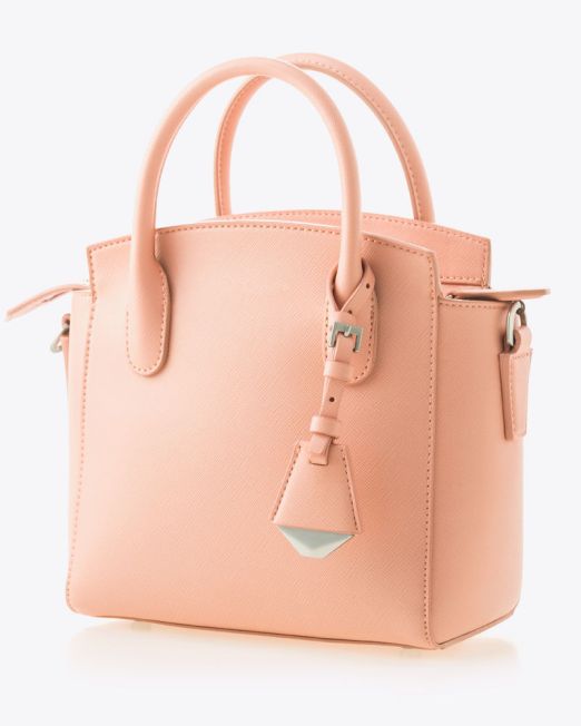 A small, structured handbag in light peach leather with two top handles, subtle texture, silver hardware, and a decorative leather tag hanging from one handle. The bag is set against a plain white background.
