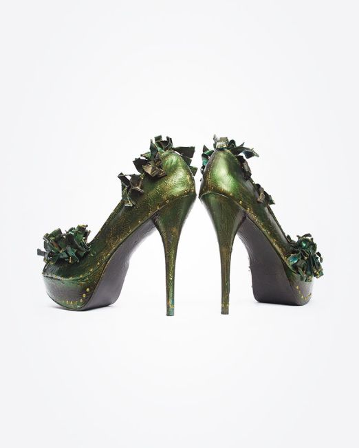 A pair of high-heeled shoes painted metallic green with decorative green ribbon accents on the front and sides, displayed on a white background with the heels facing forward.