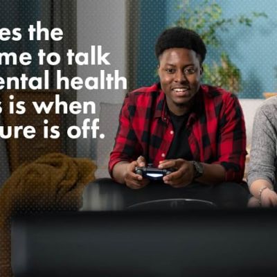 Two people smile while playing video games on a couch, with text about talking about mental health and guns.